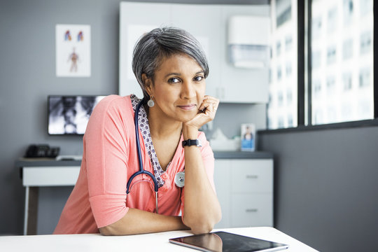 Portrait of female doctor leaning on desk in clinic