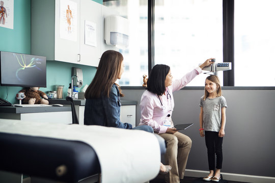 Female doctor measuring girl's height while mother sitting at clinic