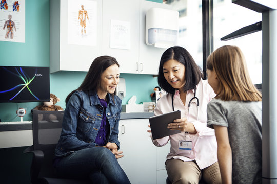Female doctor showing tablet computer to family in clinic