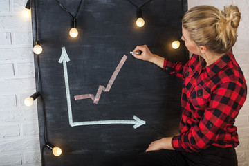 An attractive young woman with chalk at the blackboard. Graph of growth or success.