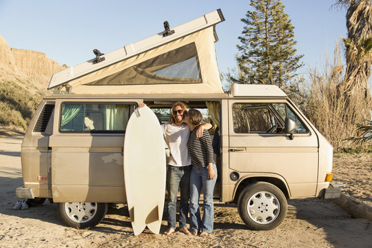 Loving woman kissing man holding surfboard in front of mini van on San Onofre State Beach