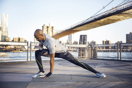 Full length of male athlete exercising on promenade with Brooklyn Bridge in background