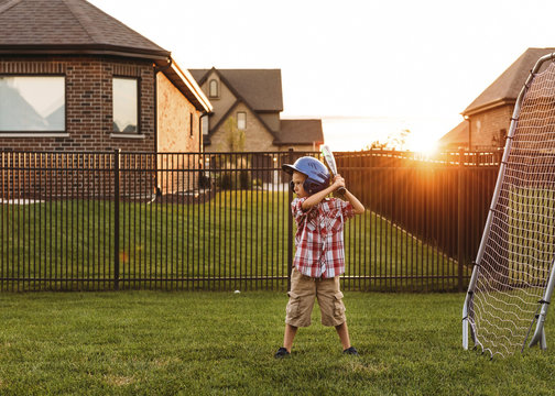 Boy playing baseball in backyard at sunset