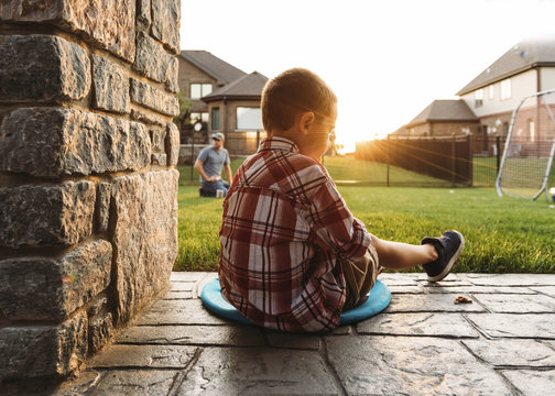 Boy sitting by column with father in background