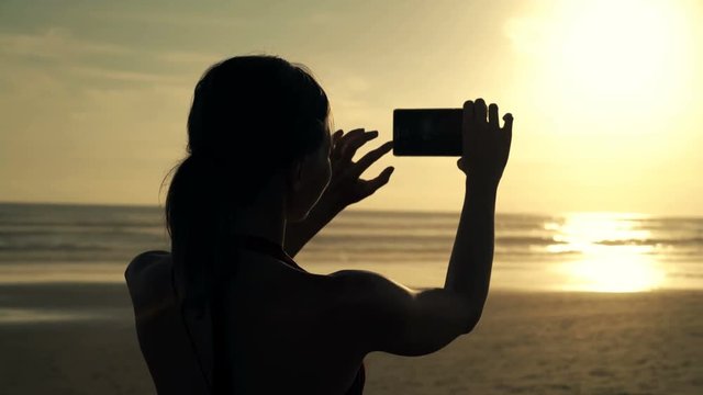 Silhouette of woman doing photo with cellphone during sunset, 4K

