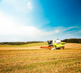 Obraz premium Working Harvesting Combine in the Oat Field. Farmland Background. Agriculture Machinery and Harvest Concept. Harvester Farm Machine. Toned Photo with Copy Space.