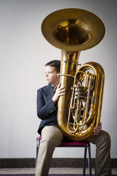 Thoughtful boy holding tuba while sitting on chair against wall