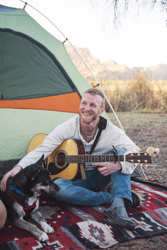 Happy man stroking dog while holding guitar outside tent