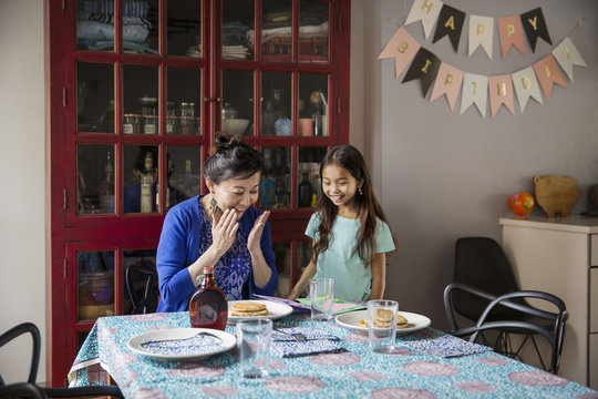Surprised mother looking at pancakes made by daughter on birthday