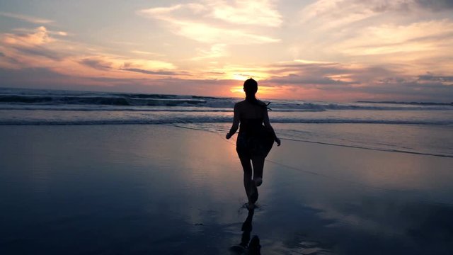 Pretty, young woman in dress running on the beach during sunset, super slow motion
