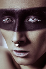 Beauty fashion shot of young man with nose rings and black strip line makeup and white eyelash....
