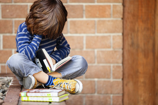Boy reading book while sitting on retaining wall