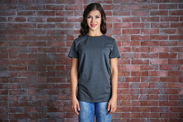Young woman in blank grey t-shirt standing against brick wall