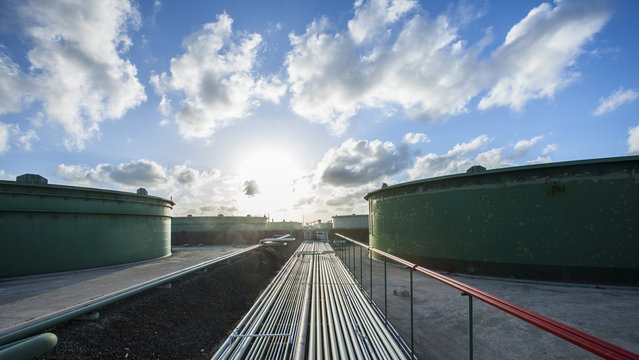 Pipelines and storage tanks at industry against cloudy sky during sunset