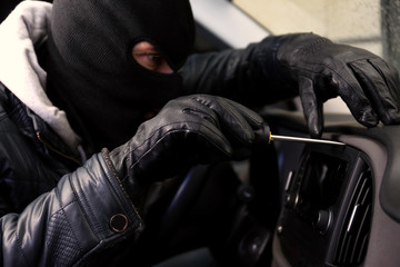 Thief in mask trying to steal car radio with screwdriver