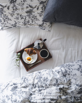 Directly above shot of breakfast tray loaded with croissant, fried egg and coffee on bed