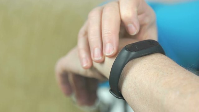 Wristband of heart rate monitor. The woman touches and looks at the wristband of pulse monitor indoors