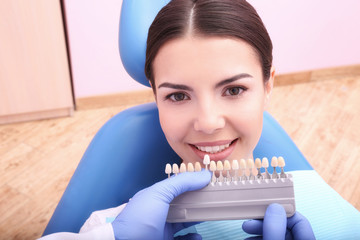 Dentist checking and selecting color of young woman's teeth
