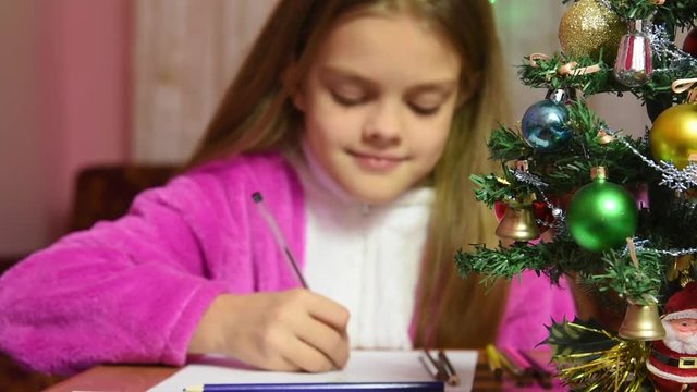Girl writing a letter to Santa Claus, the focus is on the fur-tree in front of her