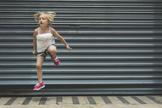 Girl jumping on sidewalk against shutter