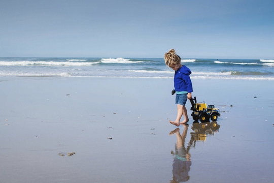 Girl pulling toy truck while walking at beach against cloudy sky