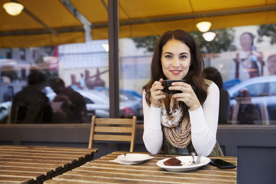 Portrait of woman holding coffee cup while sitting at sidewalk cafe