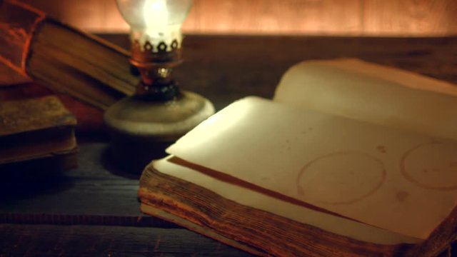 Old books and vintage oil lamp. Kerosene lantern and open old book on wooden table. 4K UHD video footage. Ultra high definition 3840X2160