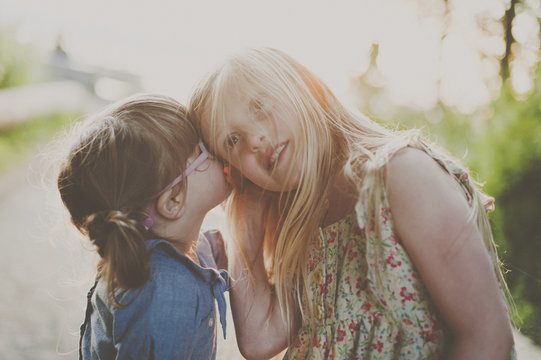 Side view of girl whispering into sister's ear on footpath