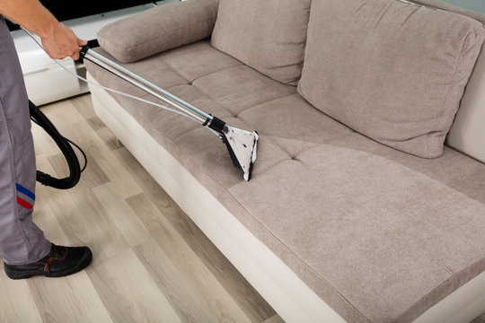 Male Worker Cleaning Sofa With Vacuum Cleaner