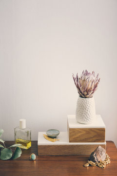 Flower vase with jewelry and beauty product arranged on table against white wall