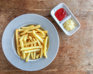 French fries on white plate with ketchup and mayonnaise sauce on wood table. top view and copy space.