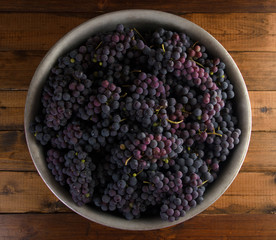 Juicy red grapes in bowl on wooden background