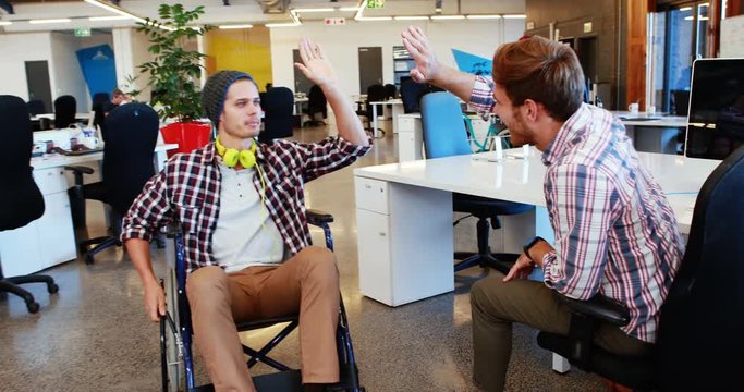 Businessman in wheelchair giving high five to coworkers