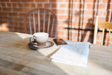 Coffee mug on a table with a phone and newspaper