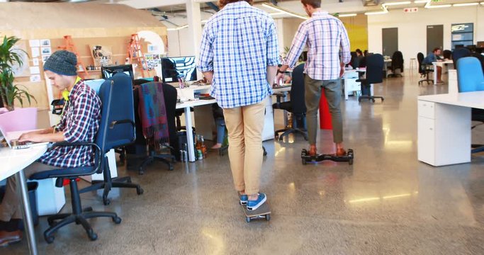 Two businessmen using hoverboard and skateboard while coworkers working