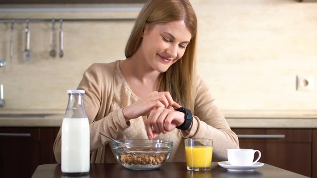 Beautiful attractive woman having breakfast, using her smart watch. Browsing Internet. Reading news.