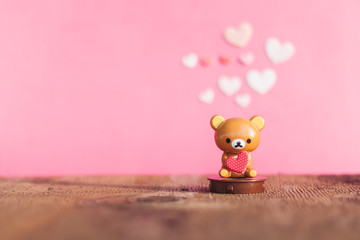 Teddy bear holding a heart on the old wood floor with pink background blur.