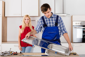 Male Plumber Fixing Stainless Steel Sink In Kitchen