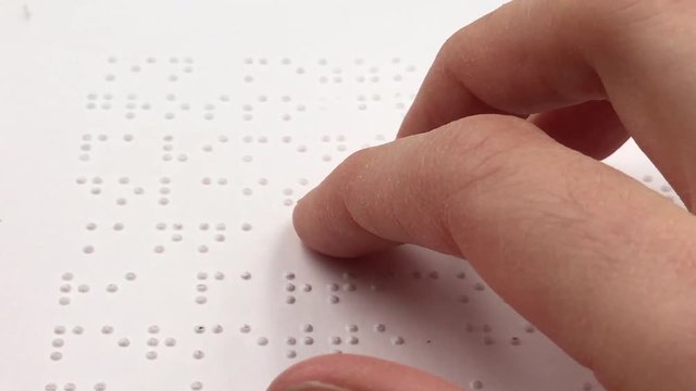 Female fingers read Braille writing on a white book