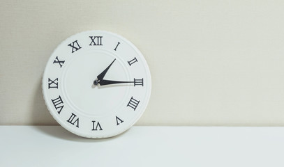 Closeup white clock for decorate show a quarter past one p.m. or 1:15 p.m. on white wood desk and cream wallpaper textured background with copy space
