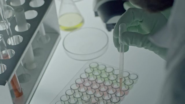 Over the shoulder shot of hands of male scientist in gloves holding pipette and pouring solutions into tray