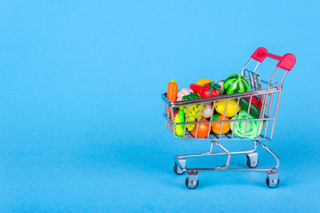 Metal shopping cart with fruits and vegetables on a blue background