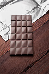 Chocolate bar in wrapper on the dark wooden background. Top view.