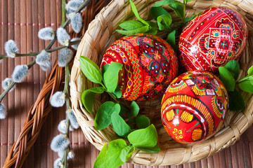 Traditional Czech easter decoration - colorful painted red eggs in wicker nest with pussycats and dogwood flower. Spring easter holiday arrangement.