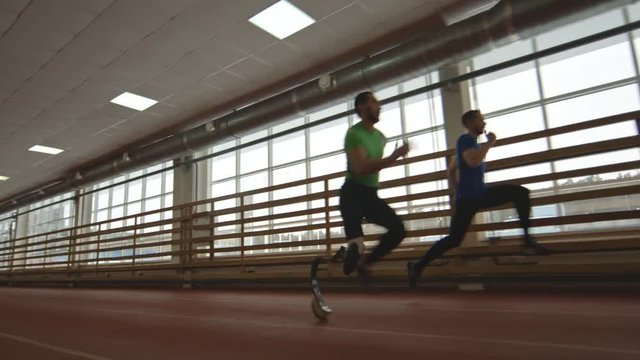 Tracking of amputee sprinter with prosthetic leg racing against fully abled sportsman at running track of indoor stadium