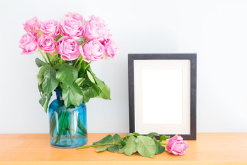 Violet fresh roses with empty photo frame on wooden shelf