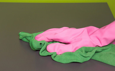 Hand in pink protective glove wiping wooden furniture with rag. Early spring cleaning or regular clean up. Maid cleans house.