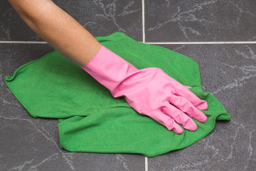 Hand in pink protective glove cleaning tiles with rag in the bathroom. Early spring cleaning or regular clean up. Maid cleans house.