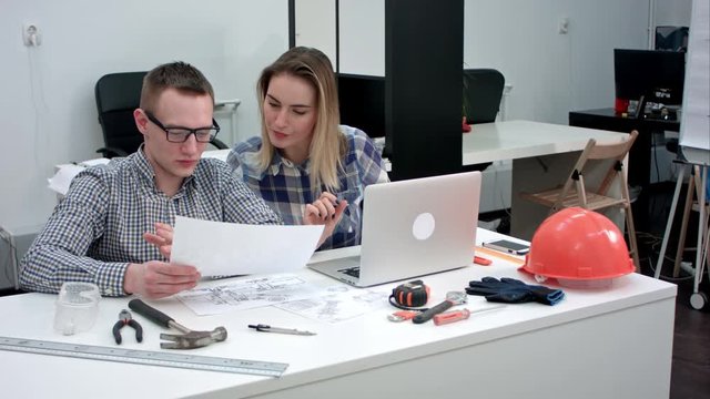 Female architect discussing drawing with her coworker while eating lunch