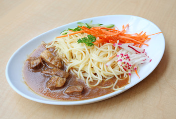 Spaghetti with steamed pork and vegetable on white plate against wooden background